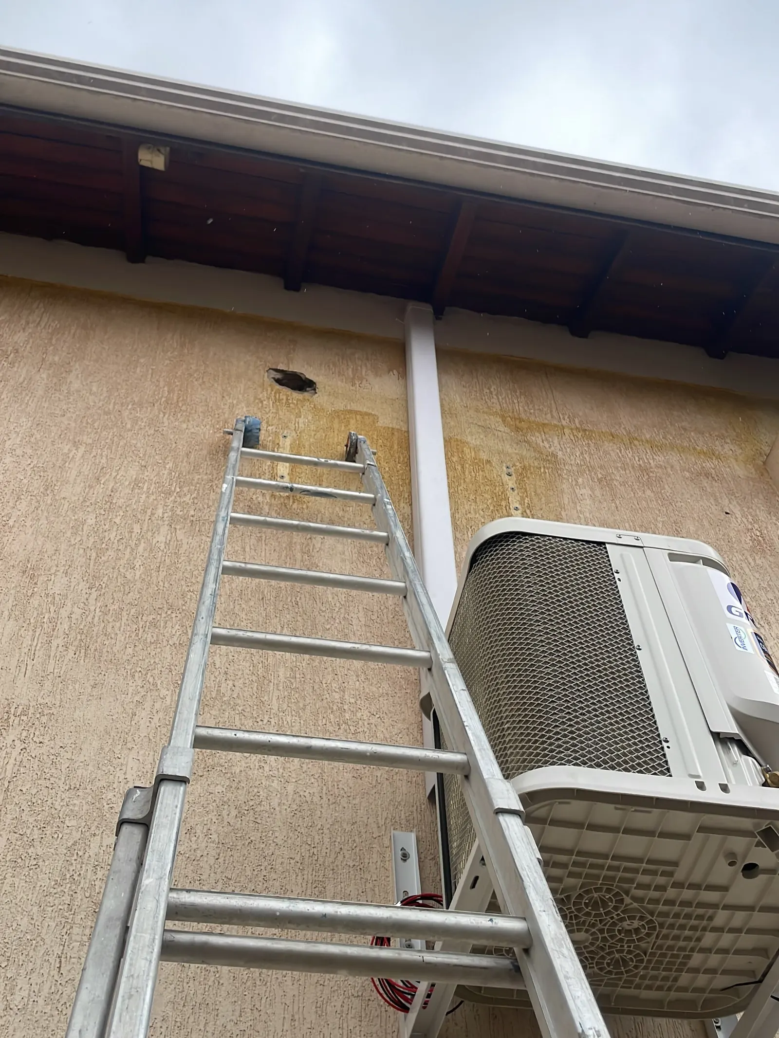 Condensadora Gree fixada no alto da parede externa, com a escada do técnico encostada